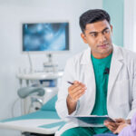 A gynecologist speaking with a woman about fibroid treatment options in a bright consultation room with laparoscopic equipment in the background.