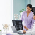 A gynecological surgeon and medical researcher reviewing pelvic imaging and a laparoscopic procedure plan in a clinical research room.